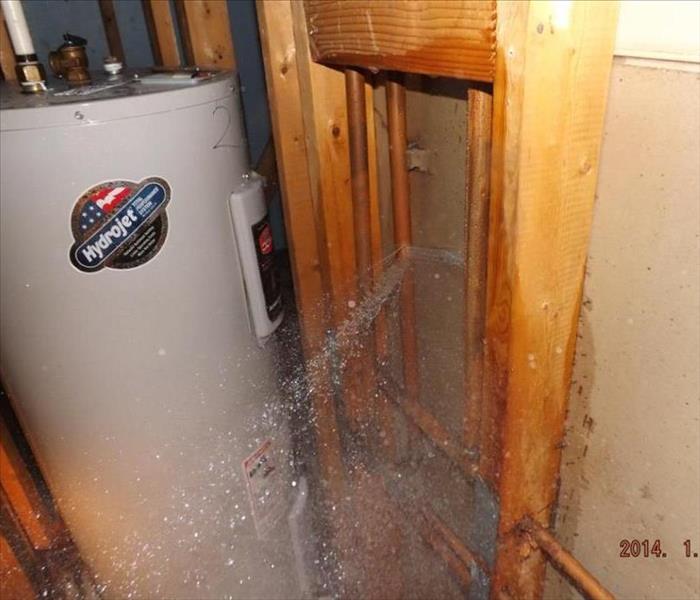 water heater against a wall with water pouring through the drywall from outside
