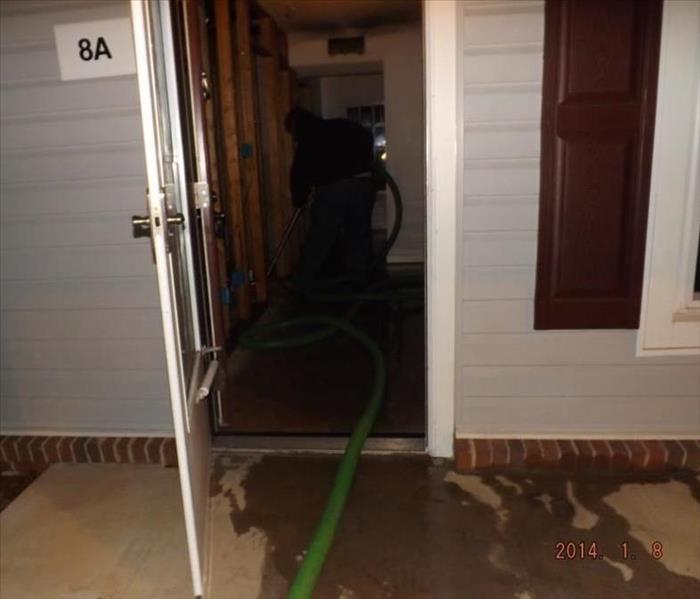 open door of a home with a green pipe running inside and water covering the patio