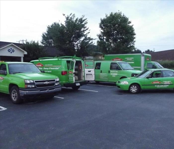 Green SERVPRO cars and vans in a parking lot